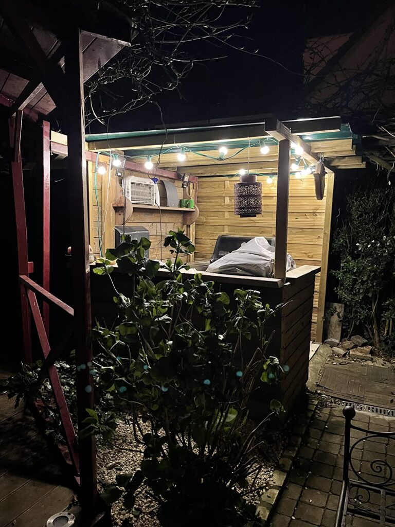 Guirlande lumineuse allumée sous un abri de jardin en bois