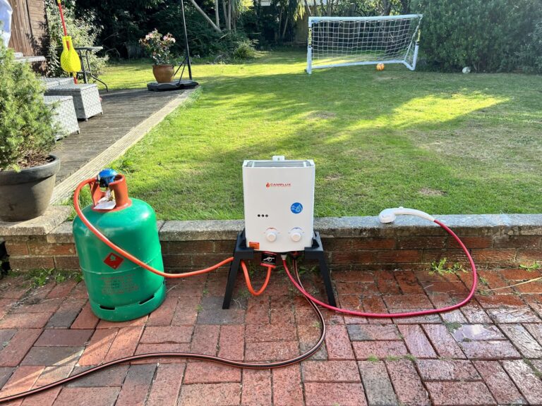 Chauffe-eau à gaz Camplux sur trépied raccordé à une bouteille de gaz dans un jardin